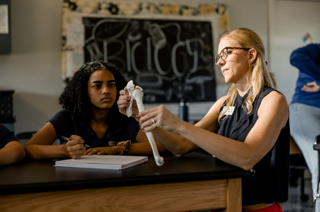A female Biology teacher at Providence Classical School in Spring, TX, instructs a female student on the bones and joint of the human shoulder.